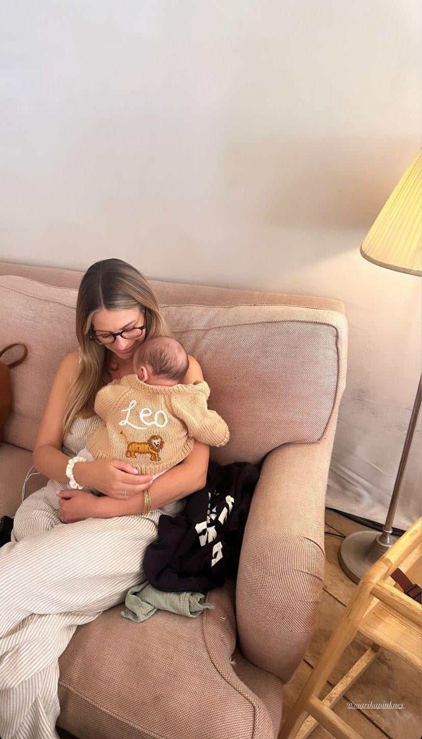 Woman holding a baby and a teddy bear with 'Leo' on it, sitting on a couch.