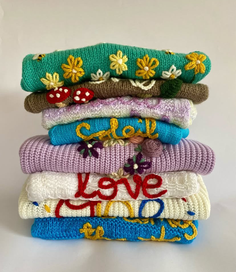 Stack of colorful embroidered sweaters on a light background